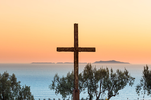 Photo of a wooden cross and the Pacific Ocean with the Channel Islands in the distance in Ventura, California, USA at sunset.