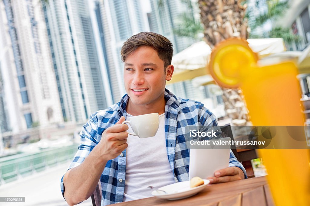 Young man drink coffee and using tablet in Dubay Young man drink coffee and using tablet in Dubay. Young man drink coffee in Dubai Marina.  iStockalypse Dubai - UAE 2015 20-24 Years Stock Photo