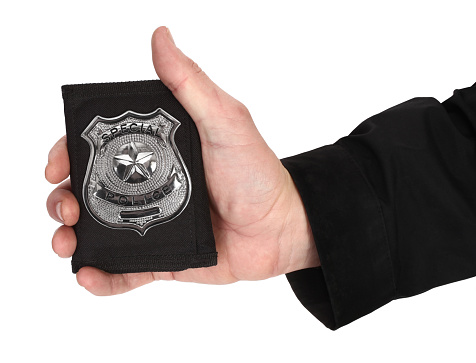 Here is man's hand, holding silver police officer badge.
