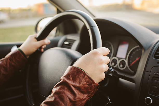 Close-up of hands on car steering wheel at 10 and 2 A woman driving a car driving test photos stock pictures, royalty-free photos & images