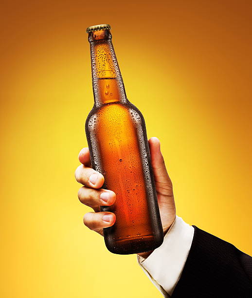 Bottle of beer in a man's hand on a yellow background.