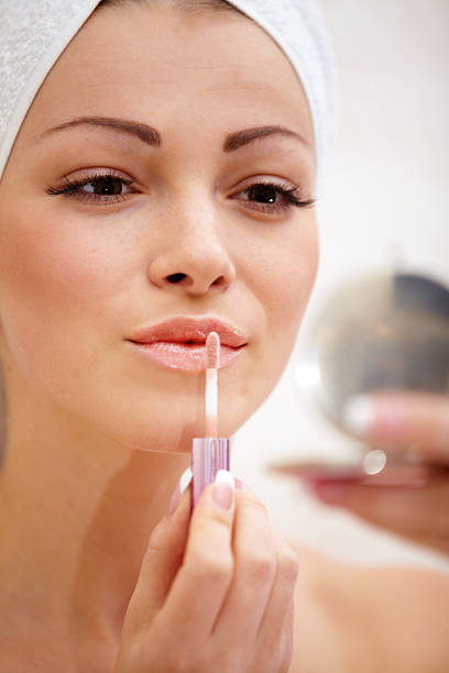 istock Woman applying lip gloss with a hand mirror 470325273