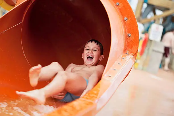 Little boy at the waterpark, going down a slide