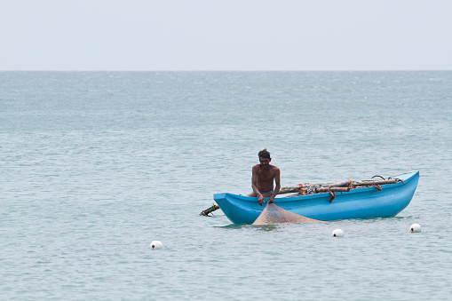 Uppuveli beach, Sri Lanka - June 9, 2014: Traditional fisherman in Uppuveli beach, Sri Lanka. He's using pendulum dugout canoe.