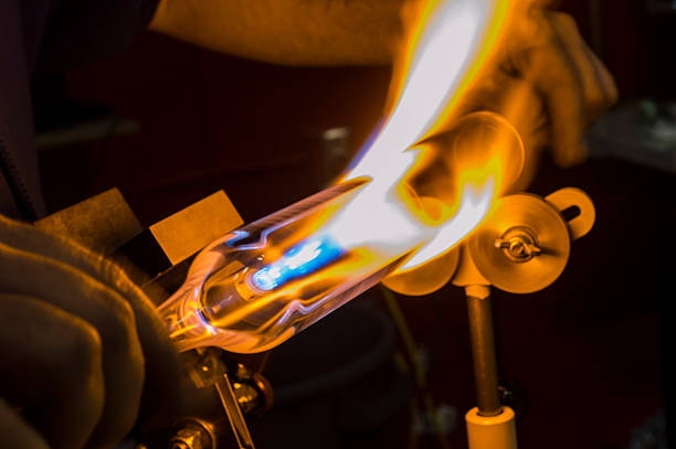 glass worker close up of a flame workers hands turning a glass tube in front of a flaming torch. hand blown glass stock pictures, royalty-free photos & images