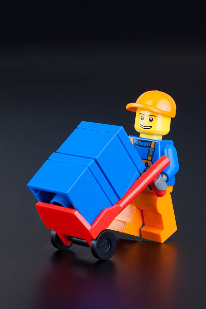 Tambov, Russian Federation - January 11, 2014: LEGO worker minifigure with hand truck and boxes on black background. Studio shot.