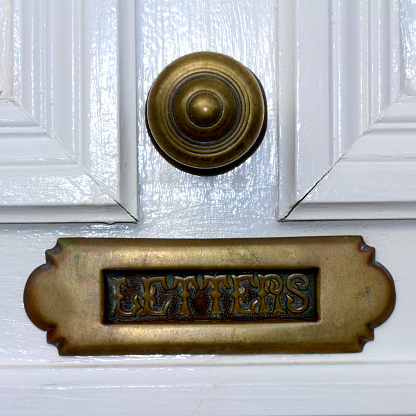 Wooden white door with bronze door-bell and letter mail drop box in Bray, Wicklow, Ireland