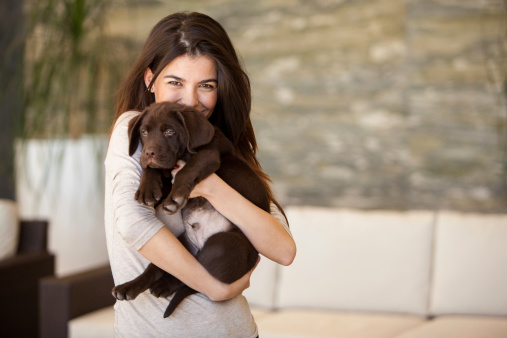 Cute young brunette hugging her Labrador dog and smiling in the living room