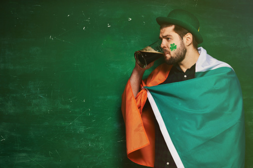 Irishman wrapped in national flag with painted clover on his face drinking stout