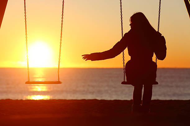 Single or divorced woman alone missing a boyfriend Single or divorced woman alone missing a boyfriend while swinging on the beach at sunset relationship difficulties stock pictures, royalty-free photos & images