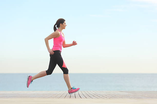 vista lateral de uma mulher correr na praia - running women jogging profile imagens e fotografias de stock