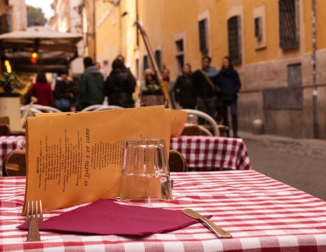 Close-up on a table of an outdoor Italian restaurant with medieval alley and people walking in the background