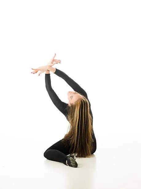back view of ballerina sitting on floor holding hands up crossed, on white background