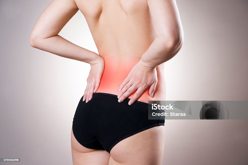 Pain in lower back of women Pain in lower back of women on gray background. Caring for the female body. Red dot Lower Back Stock Photo