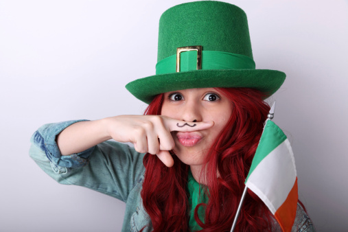 Beautiful teenage girl with leprechaun's hat, finger printed moustache and Irish flag