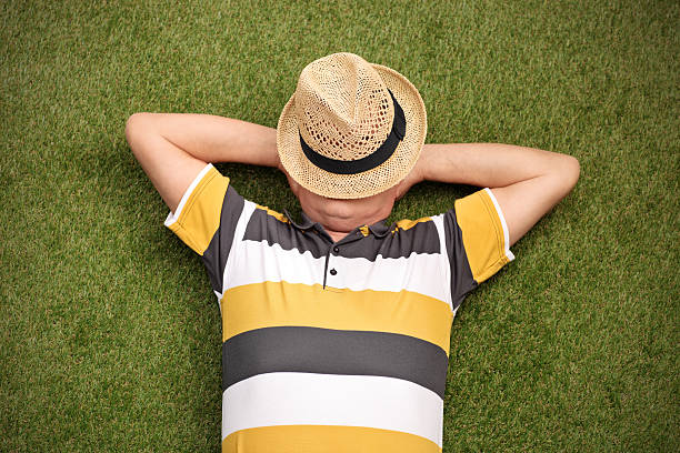 Senior gentleman lying in a field on green grass with the hat over his face