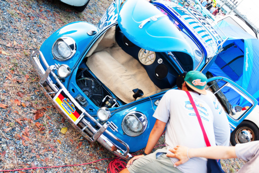 Bangkok, Thailand - February, 15th 2014: Two men are connecting mobile with old blue VW Beetle. Front bonnet is open, inside are speaker. Men are connecting cable to phone. Seen in Bangkok.