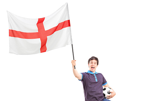 Euphoric young football fan holding an English flag and football isolated on white background