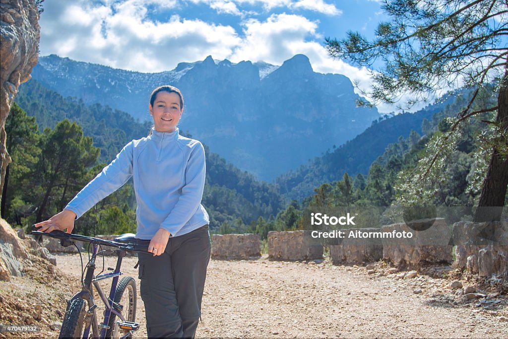 Woman biking Young woman riding a bike on track with mountains at background 2015 Stock Photo