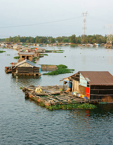 My Tho, Vietnam - February 13, 2012: Man sails on ratty boat with fish farm raft houses floating on Mekong river with Rach Mieu Bridge in background on February 13, 2012 in My Tho, Vietnam. 