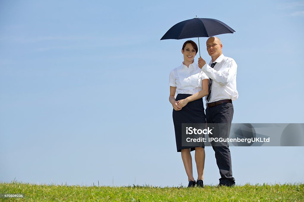 Portrait of businessman and businesswoman under umbrella in park 20-29 Years Stock Photo