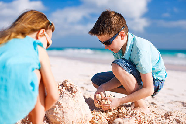 Two kids building sand castle Brother and sister building sand castle at tropical beach sandcastle structure stock pictures, royalty-free photos & images