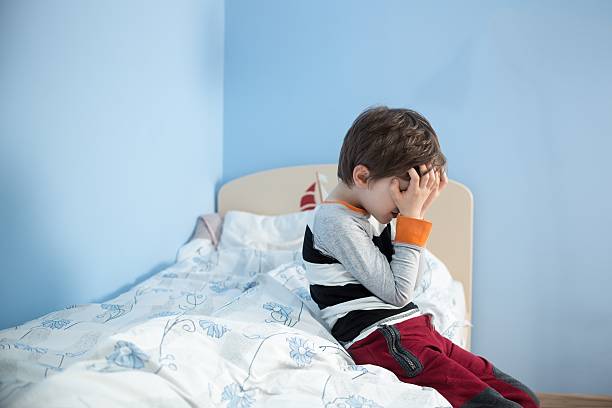 Sad little boy sitting on the edge of his bed. stock photo