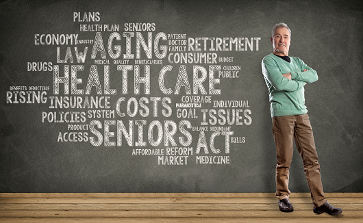 Senior Man, Health Care Word Cloud on Blackboard background. Happy Man standing on wooden floor, against a Blackboard background