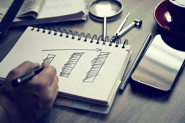 Businessman's hand drawing progressive bar graph on spiral notebook that represents the business growth. Close-up shot of financial data and statistics.