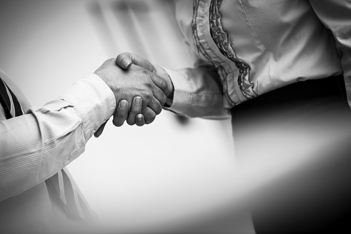 Close-up of businessman and businesswoman shaking hands in the office. Image is in black and white.