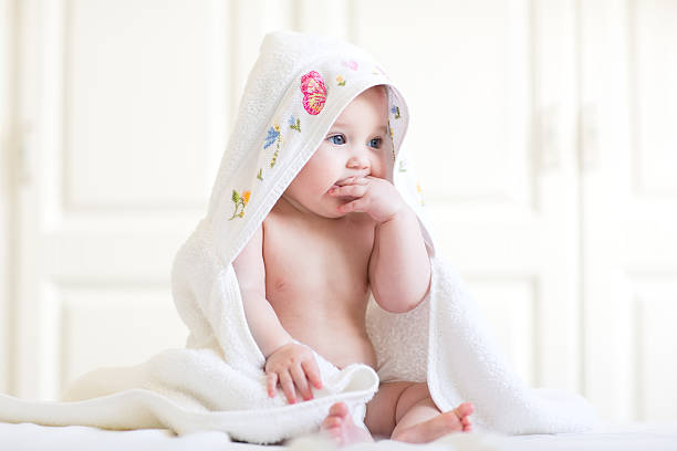 adorável bebê menina sentada em uma toalha com capuz depois de banho - baby cheerful child blanket - fotografias e filmes do acervo