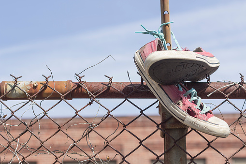 Pair of old worn classic sneakers hang from rusty chain link fence