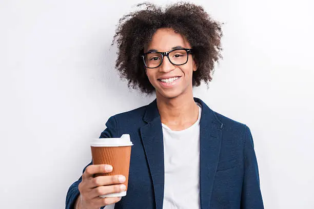 Handsome young African man holding a cup of coffee and smiling while standing against grey background