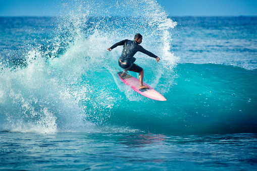 A young native Hawaii man surfing on the wave of Poipu Beach, on the island of Kauai, Hawaii, USA. He is on a pink surfboard and making a turn on the wave in the aqua sea of Kauai. Photographed in horizontal format with copy space available.