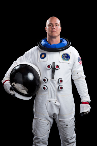 This is a portrait of an astronaut holding a helmet. The background is a pure black allowing for endless copy above. The Saturn and Earth patches are fake and were created in Photoshop.