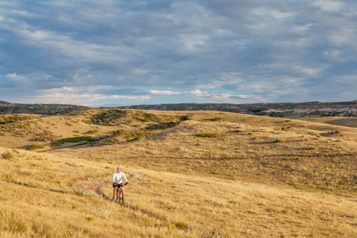 a lonely male biking over rolling prairie illuminated by sunrise at Soapston Prairie Natural Area in northern Colorado near Fort Collins, late summer