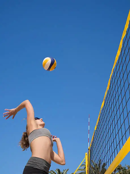 Attractive sporty young woman is jumping and smashes the volleyball over the net