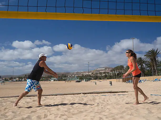 A man and a woman are playing beachvolleyball on the beach. The man is giving a forehand pass to the woman.