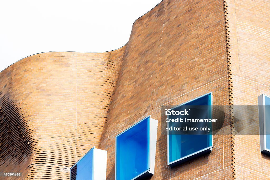 Top part abstract curve brick building with squre blue windows Sydney, Australia - April 12, 2015: Sydney Ultimo Road Dr Chau Chak Wing Building. It is a Business School building of the University of Technology in Sydney, Australia. It is building designed by Canadian-American architect Frank Gehry. The tower is named after Dr Chau Chak Wing, an Australian-Chinese businessman and philanthropist The 12-storey tower provides teaching, learning, research and office accommodation. Low angle view top part of curve brick building with blue sky reflection on windows.  2015 Stock Photo