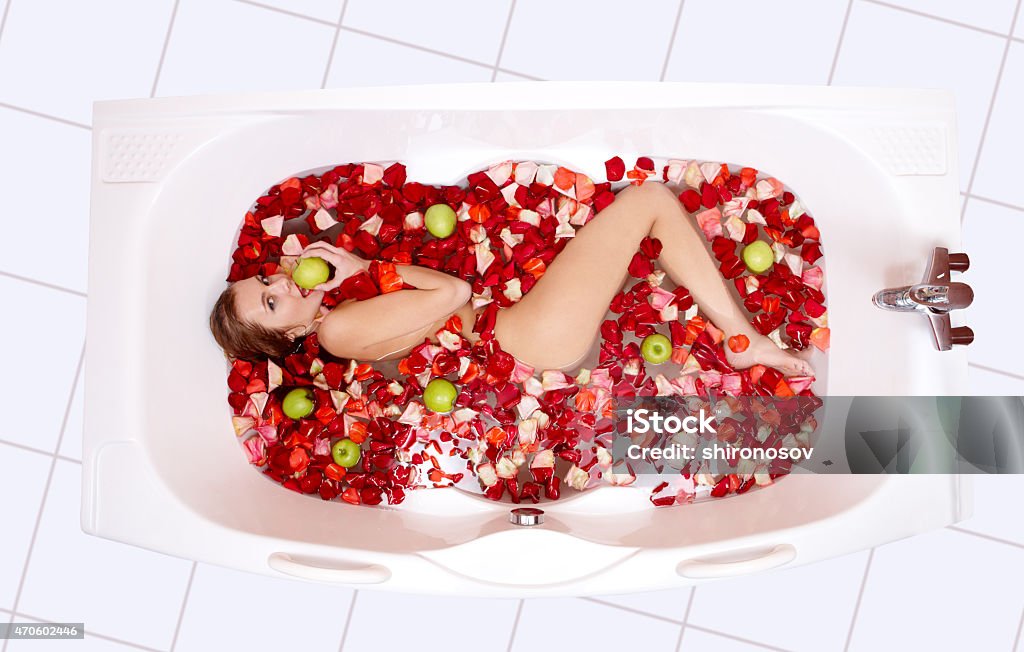 In the bathroom Portrait of attractive woman lying in the bathtub and eating apple 2015 Stock Photo