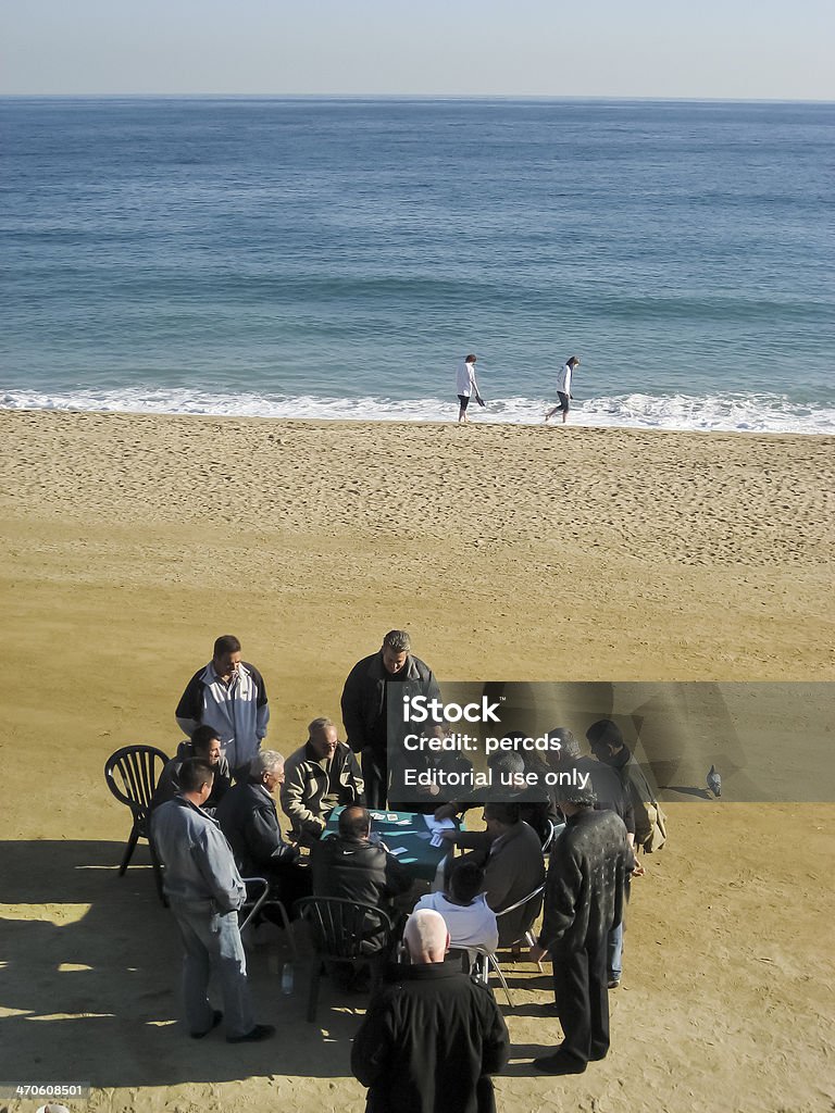 Playing cards in Barceloneta beach Barcelona, spain-december 13, 2007: group of men, most of them senior,  playing cards or watching the play in Barceloneta beach, Barcelona, a winter afternoon. Two people walking by the sea in the background. Active Seniors Stock Photo