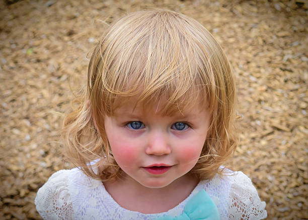 Doll-like Child A gorgeous blue-eyed, blonde girl at a park playground.  rosy cheeks stock pictures, royalty-free photos & images