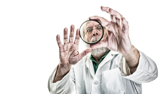 A kooky, tangled hair research scientist or medical professional with a wide-eyed, delighted expression on his face is staring through the circular glass lens he is holding out toward the camera. Looks like he has discovered something very important! He is a balding senior adult man with a gray beard and mustache. He is wearing a white lab coat. Canon 5D Mark III.
