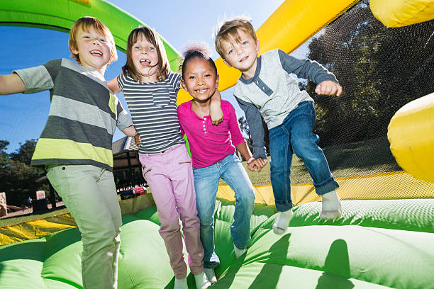 4 つの多民族の子供達が遊んでお城形トランポリン - celebration inflatable excitement concepts ストックフォトと画像