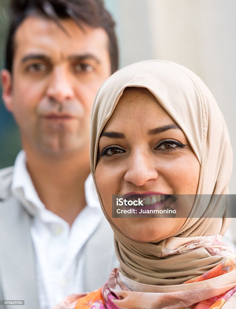 Smiling middle eastern couple Smiling middle eastern couple looking at the camera, she is wearing a muslim hijab, he is serious in the background 2015 Stock Photo
