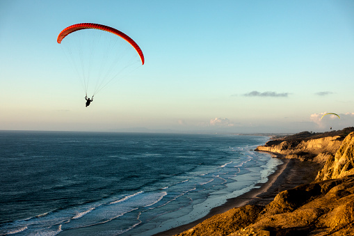 Paraglider flying over ocean cliffs at sunset