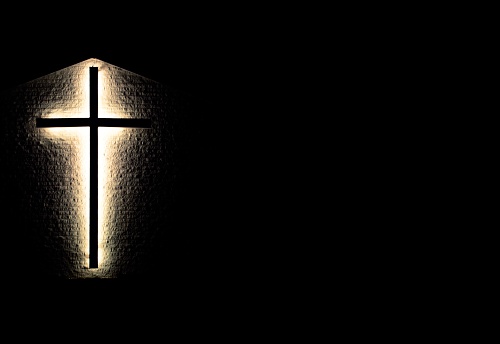  Illuminated cross at night set against a brick wall in horizontal orientation with copy space.