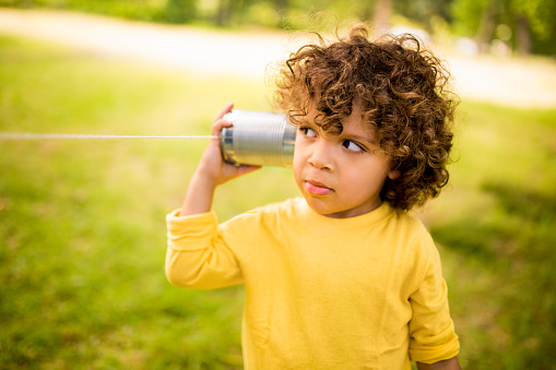 Interested little boy listening to sound vibrations coming through a tin can phone in a park