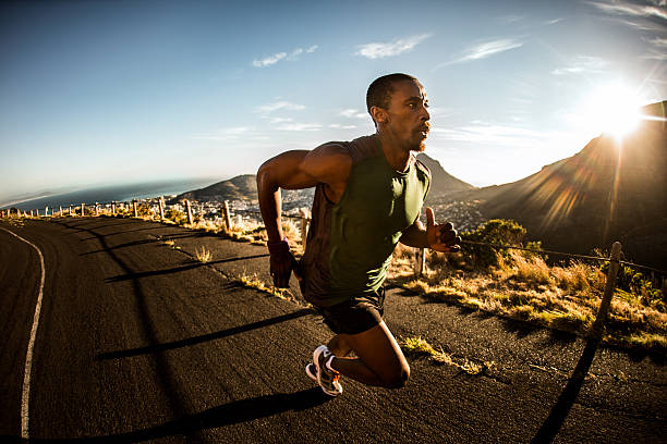 Wide angle shot of an athlete sprinting along a road outdoors on a bright morning in his fitness training