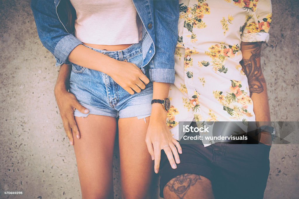 Retro style hipster couple standing affectionately alongside eac Cropped midsection of a hipster couple standing close together and leaning against a wall in retro style clothing Tattoo Stock Photo